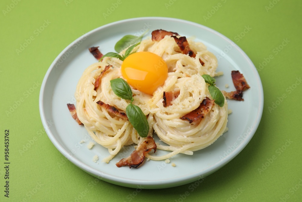 Delicious pasta Carbonara with egg yolk, bacon and basil on green table, closeup Delicious pasta Carbonara with egg yolk, bacon and basil on green table, closeup