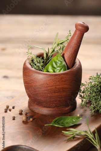 Different fresh herbs in mortar with pestle on wooden table
