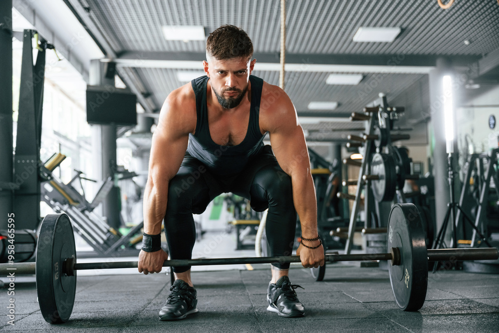 Lifts a barbell. Strong muscular man is working out in the gym Lifts a barbell. Strong muscular man is working out in the gym