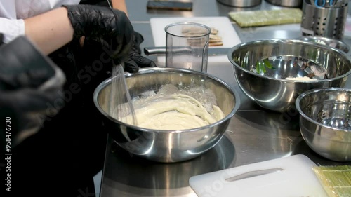 making vanilla sauce in a pot whisking white sauce in an iron bowl in the kitchen, chef wearing black gloves photo