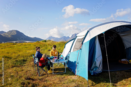 Happy family with three kids, wild camping in Norway summertime, people having breakfast and coffee on a cliff next to a fjord in Norway