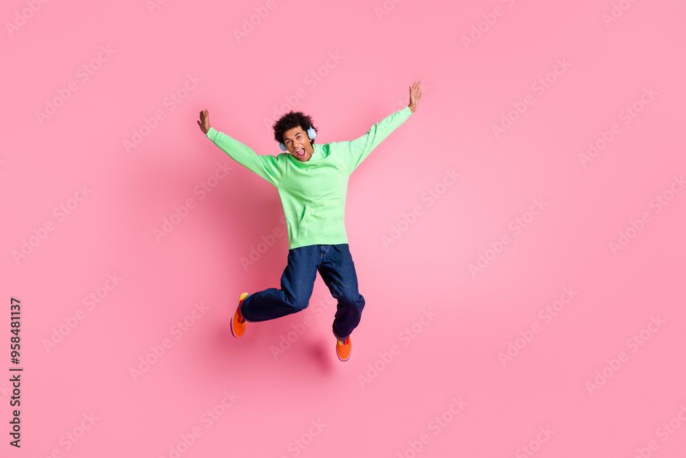 Full body portrait of cool young man headphones jumping wear green hoodie isolated on pink color background Full body portrait of cool young man headphones jumping wear green hoodie isolated on pink color background