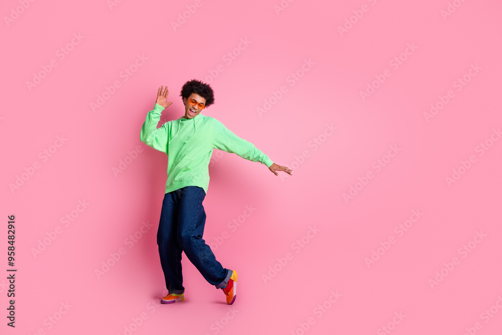 Full size photo of nice young man have fun dancing wear green hoodie isolated on pink color background Full size photo of nice young man have fun dancing wear green hoodie isolated on pink color background