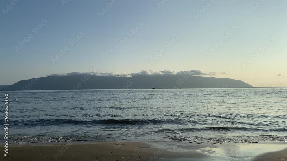 A young millennial woman in straight pants and a white t-shirt is dreamily walking along the seashore on the sand. Concept of spending time alone, unity with nature, lifestyle of real people, vacation A young millennial woman in straight pants and a white t-shirt is dreamily walking along the seashore on the sand. Concept of spending time alone, unity with nature, lifestyle of real people, vacation