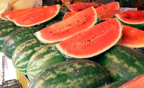 whole watermelons and melons at a market, with several slices of ripe watermelon. Ideal for food, agriculture, or summer-themed projects, captures the freshness of seasonal fruits
