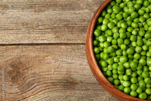 Fresh green peas in bowl on wooden table, top view. Space for text