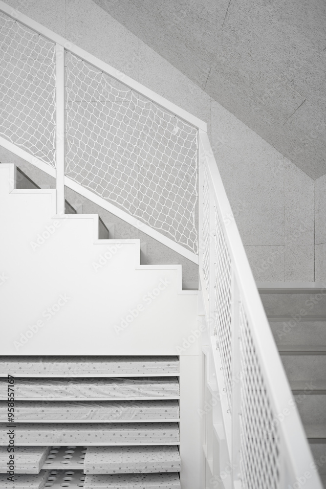 Fototapeta premium White staircase with netted railing, minimalist design featuring clean geometric lines, bright lighting, and abstract forms, blending modern architecture with functional simplicity.