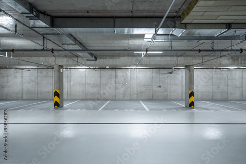 A well-lit underground parking garage with empty parking spaces, concrete columns, and visible overhead pipes, exuding an industrial atmosphere.