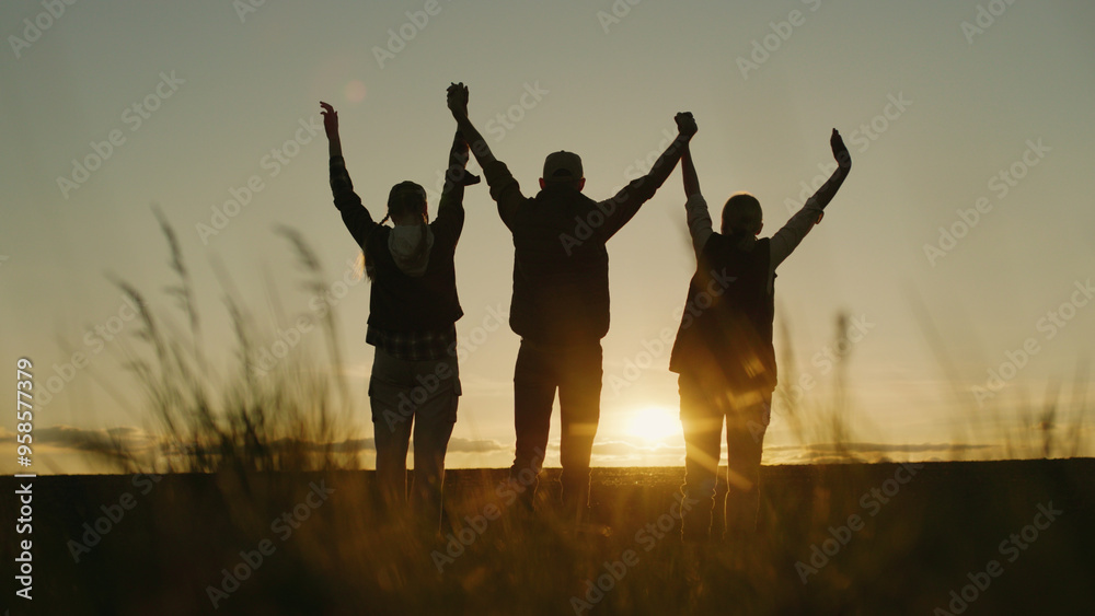 Against the backdrop of the setting sun, a family of farmers raises their hands in a confident sign of success while standing in their field. Against the backdrop of the setting sun, a family of farmers raises their hands in a confident sign of success while standing in their field.