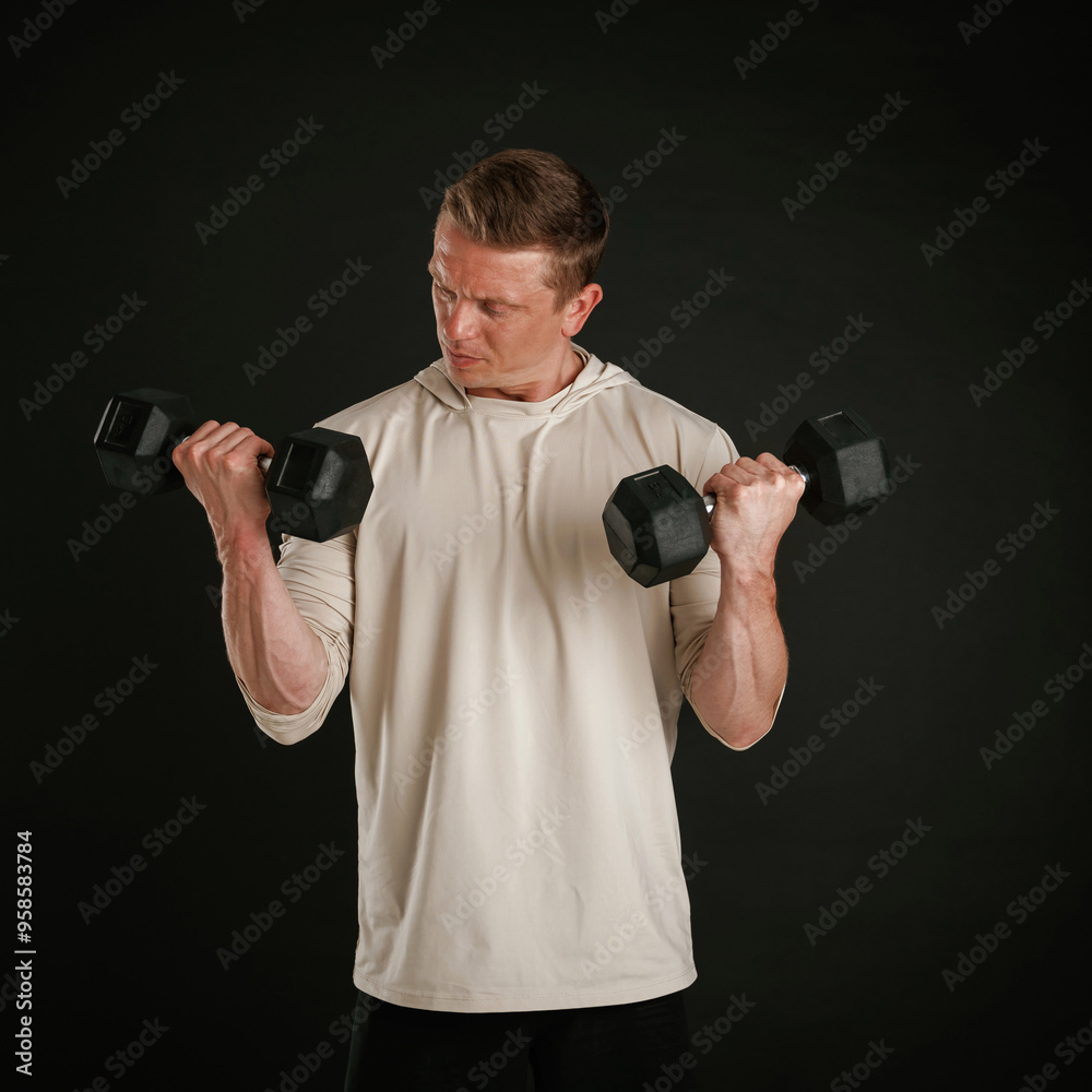 Powerful sportsman is holding dumbbells. Against background in the studio Powerful sportsman is holding dumbbells. Against background in the studio