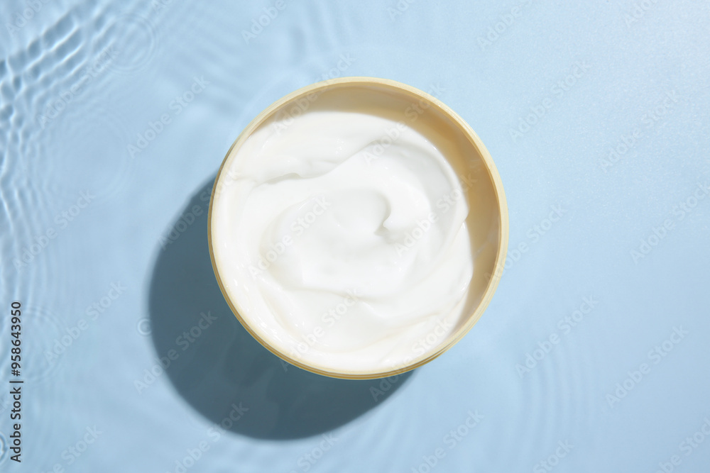 Cosmetic product. Jar with cream in water on light blue background, top view Cosmetic product. Jar with cream in water on light blue background, top view