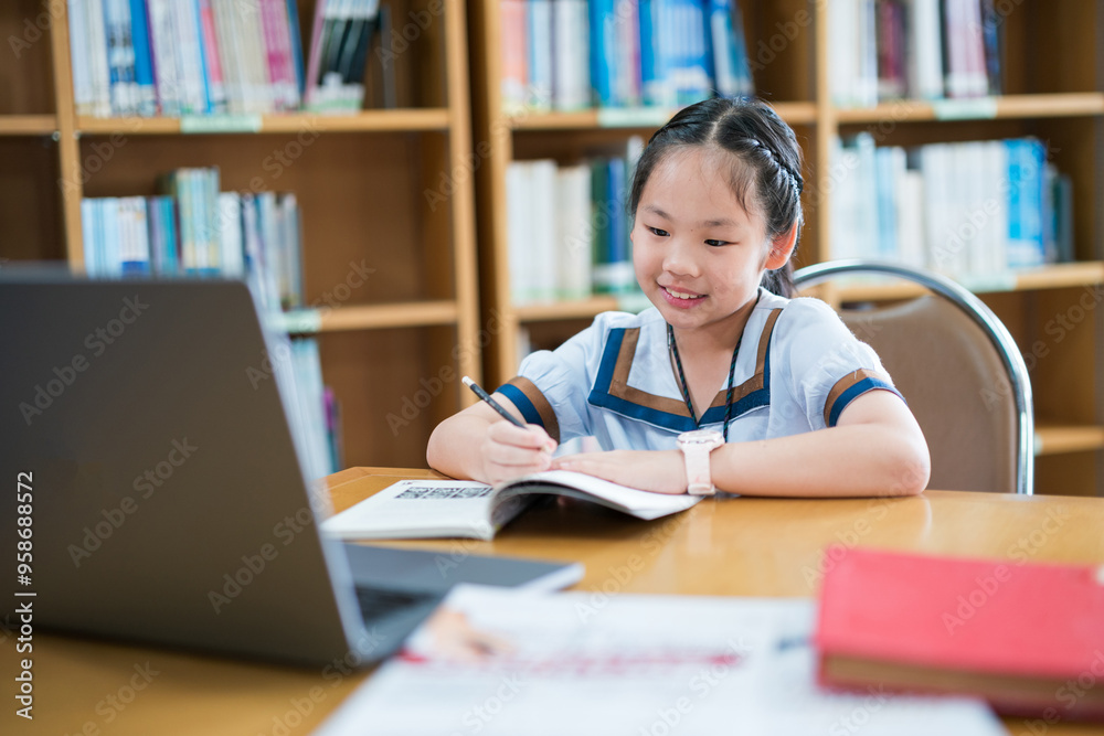 Young girl in a school uniform studying alone at a desk, writing in a notebook while referencing a laptop, smiling and focused, surrounded by bookshelves, capturing a moment of independent learning Young girl in a school uniform studying alone at a desk, writing in a notebook while referencing a laptop, smiling and focused, surrounded by bookshelves, capturing a moment of independent learning