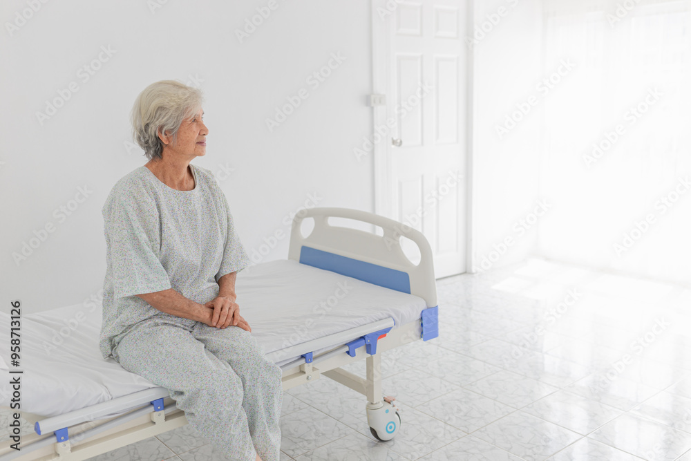 Obraz premium Elderly patient woman sitting on a hospital bed. The image conveys a sense of solitude and contemplation, as the patient appears to be reflecting during her stay in the healthcare facility.