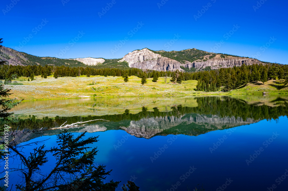 Yellowstone National Park's Trout Lake with beautiful reflections in the water and sun burst in the sky with mountains in the background Yellowstone National Park's Trout Lake with beautiful reflections in the water and sun burst in the sky with mountains in the background