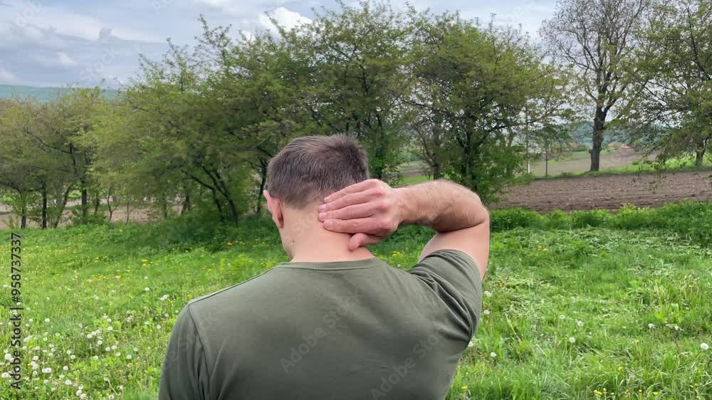 Man standing in a field massages his neck while feeling discomfort and tension in the surrounding nature Man standing in a field massages his neck while feeling discomfort and tension in the surrounding nature