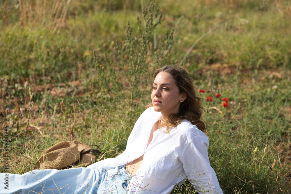 pretty young blonde woman in white shirt, jeans and boots is sitting on the fresh green grass surrounded by poppies while sunbathing. Photos in nature. pretty young blonde woman in white shirt, jeans and boots is sitting on the fresh green grass surrounded by poppies while sunbathing. Photos in nature.