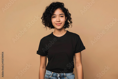 A young Hispanic woman with curly hair wearing a black shirt and jeans, smiling softly against a warm beige background.