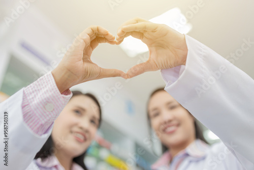 Healthcare professionals forming heart shape with hands. Blurred smiling faces of female pharmacists in white coats. Compassionate medical care concept in pharmacy setting. unity and teamwork.