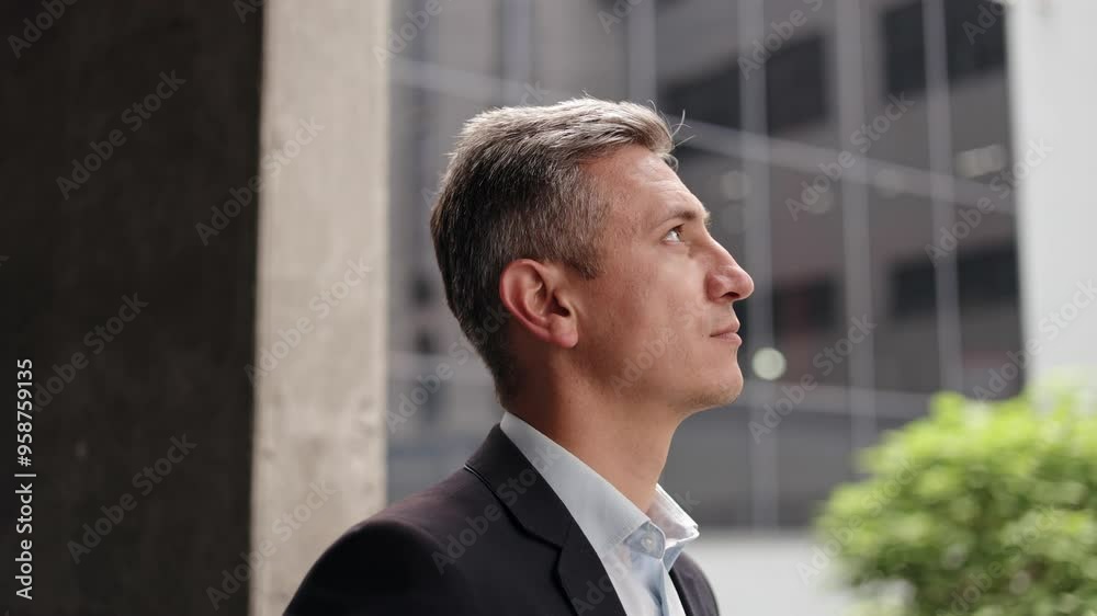 A middle-aged businessman with grey hair, wearing a suit, stands in a modern city center, looking thoughtfully into the distance. He projects an image of business success, leadership, ambition. A middle-aged businessman with grey hair, wearing a suit, stands in a modern city center, looking thoughtfully into the distance. He projects an image of business success, leadership, ambition.