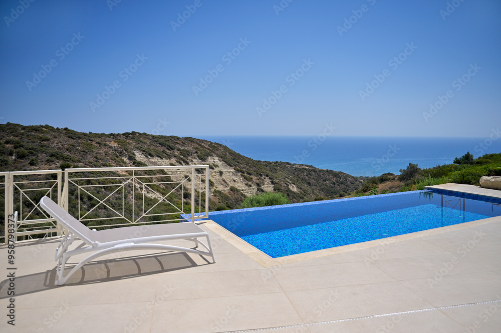 Fototapeta premium The white sun lounger was the scene's centrepiece, perfectly positioned beside the inviting pool. The summer landscape was idyllic, and the distant sea view added to the moment's tranquillity.