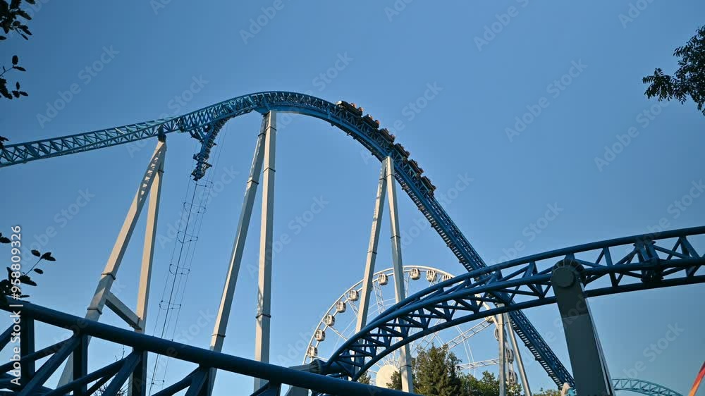 Roller coaster people ride in an amusement park against the blue sky. Active recreation on the rides with the whole family. Adrenaline and risk on the example of a downhill slide. Roller coaster people ride in an amusement park against the blue sky. Active recreation on the rides with the whole family. Adrenaline and risk on the example of a downhill slide.