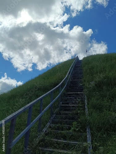 Bubiai hill during sunny day. Small hill. Grass is growing on hill. Staircase leading to the top. Sunny day with white and gray clouds in sky. Nature. Bubiu piliakalnis. photo