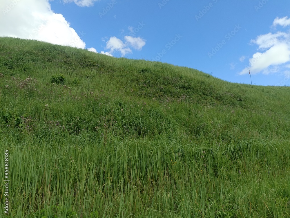 Bubiai hill during sunny day. Small hill. Grass is growing on hill. Staircase leading to the top. Sunny day with white and gray clouds in sky. Nature. Bubiu piliakalnis. Bubiai hill during sunny day. Small hill. Grass is growing on hill. Staircase leading to the top. Sunny day with white and gray clouds in sky. Nature. Bubiu piliakalnis.