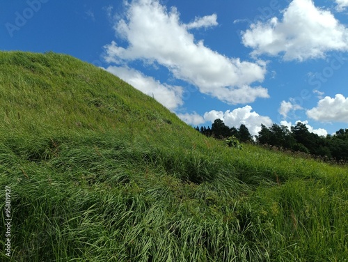 Bubiai hill during sunny day. Small hill. Grass is growing on hill. Staircase leading to the top. Sunny day with white and gray clouds in sky. Nature. Bubiu piliakalnis. photo