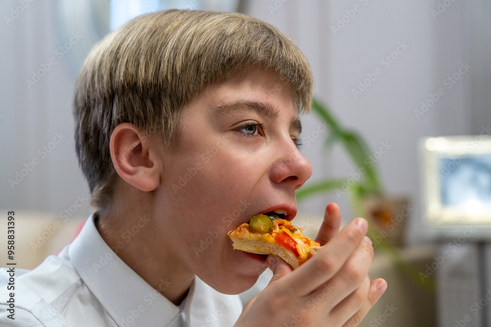 A young boy takes a bite of pizza topped with green olives while seated in a cozy indoor setting A young boy takes a bite of pizza topped with green olives while seated in a cozy indoor setting