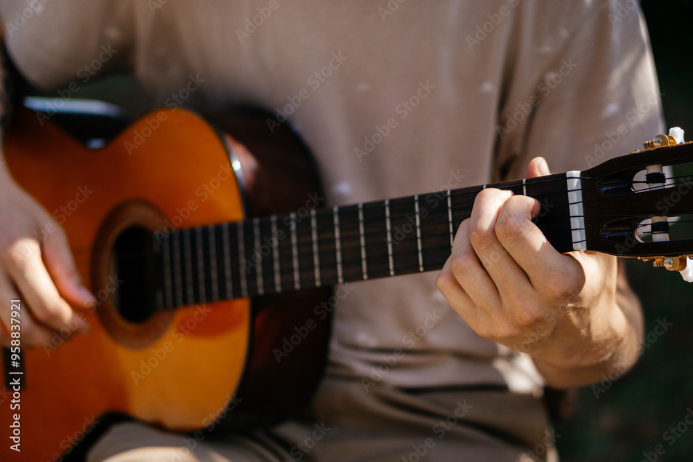 Fototapeta premium young man is playing acoustic guitar outside on summer