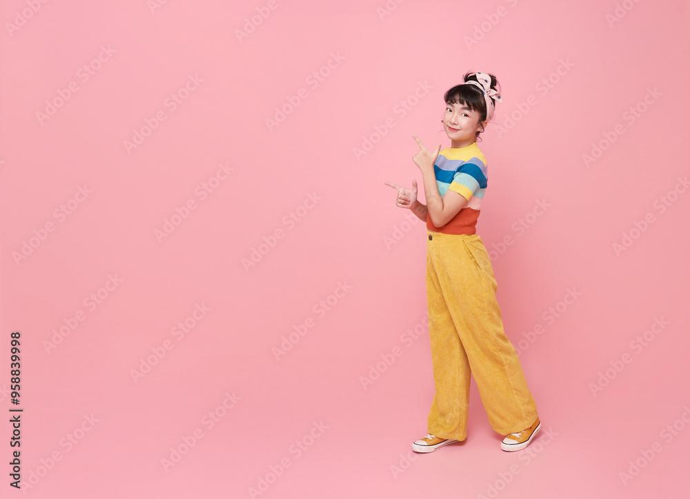 Smiling little asian girl looking and pointing finger shows place for your advertising text Isolated on pink background. Smiling little asian girl looking and pointing finger shows place for your advertising text Isolated on pink background.