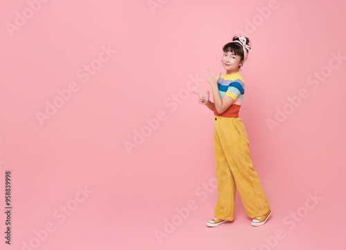 Smiling little asian girl looking and pointing finger shows place for your advertising text Isolated on pink background.