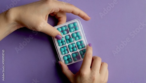 Female hand holding a plastic pill organizer against a lilac background.