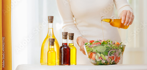 Woman hold glasses bottle with fresh extra virgin, sunflower oil pouring into bowl of vegetable salad. Concept banner eco super food for life