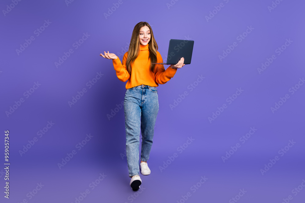 Photo of charming blonde hair cute happy smile girl in orange pullover studying speaking online holding netbook isolated on violet color background Photo of charming blonde hair cute happy smile girl in orange pullover studying speaking online holding netbook isolated on violet color background