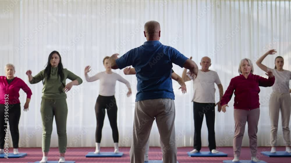 Group of Caucasian People of Diverse Ages Following Coach in Standing Alternating Arm Stretch Exercise in Fitness Class in Slow Motion. Concept of Recreation, Coordination, Consistency, Discipline Group of Caucasian People of Diverse Ages Following Coach in Standing Alternating Arm Stretch Exercise in Fitness Class in Slow Motion. Concept of Recreation, Coordination, Consistency, Discipline