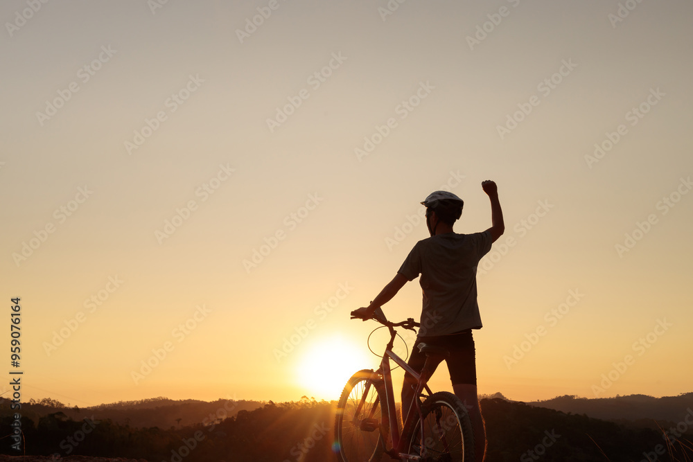 Fototapeta premium Mountain biker takes a break at sunset, raising an arm in celebration. The stunning sunset and peaceful atmosphere evoke a sense of achievement, freedom, and passion for outdoor adventure