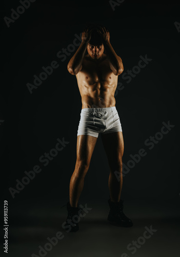 Fit muscular man striking a pose in white shorts and boots in a dark studio setting, showcasing strength and determination.