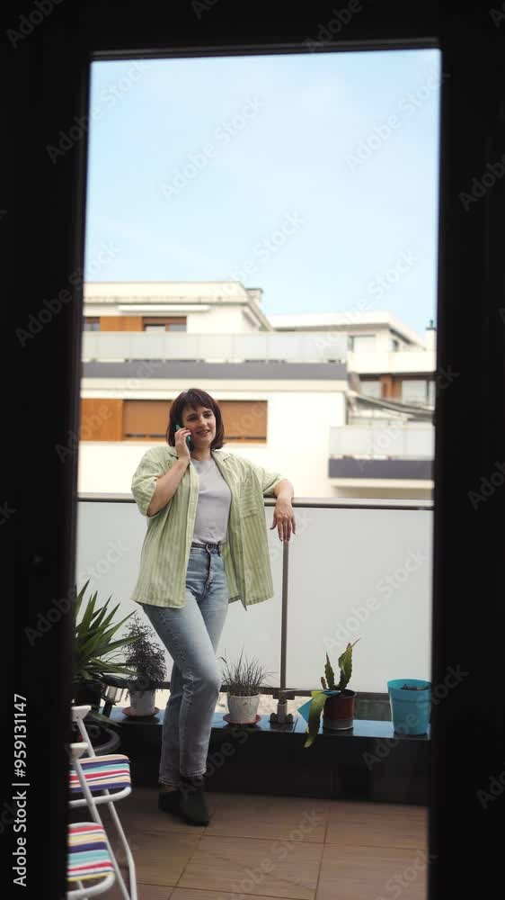A woman stands on a balcony in an apartment and calls on a mobile phone, talking on a mobile phone, smile, pleasant call, communication, connection, mobile network, home environment A woman stands on a balcony in an apartment and calls on a mobile phone, talking on a mobile phone, smile, pleasant call, communication, connection, mobile network, home environment