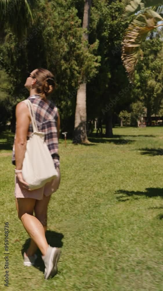 Vertical video. Woman walks away on a Grassy Path surrounded by Dense Tropical Foliage, with her Bag swinging gently by her side. Vertical video. Woman walks away on a Grassy Path surrounded by Dense Tropical Foliage, with her Bag swinging gently by her side.