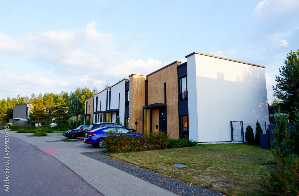 Obraz premium Modern townhouses in a residential area. New apartment buildings with green outdoor facilities in sustainable enviroment. Street with Two-story townhouses. Townhouse along sidewalk with green lawn.