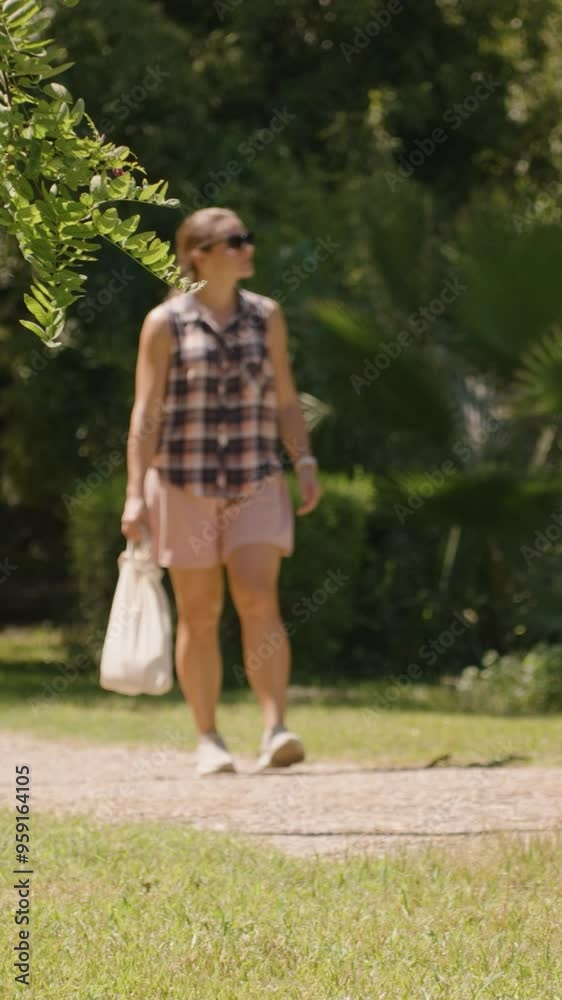 Vertical video. Woman walks along a Sunlit Path in a Park, surrounded by Lush Greenery and Tall Reeds. Slow motion. Vertical video. Woman walks along a Sunlit Path in a Park, surrounded by Lush Greenery and Tall Reeds. Slow motion.