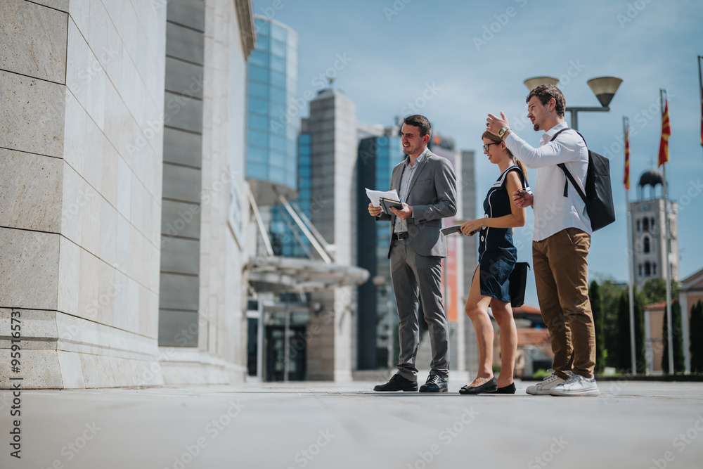 Three professionals converse about business plans in a modern urban setting, highlighting teamwork and strategy in the midst of city architecture. Three professionals converse about business plans in a modern urban setting, highlighting teamwork and strategy in the midst of city architecture.