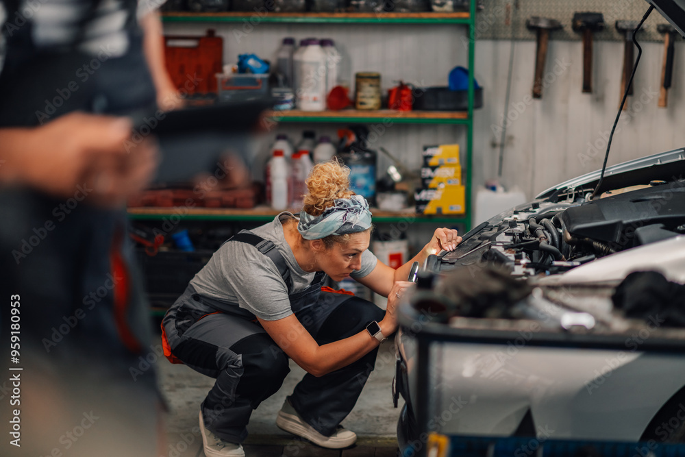 Fototapeta premium Female mechanic crouching and looking for problem under hood at workshop