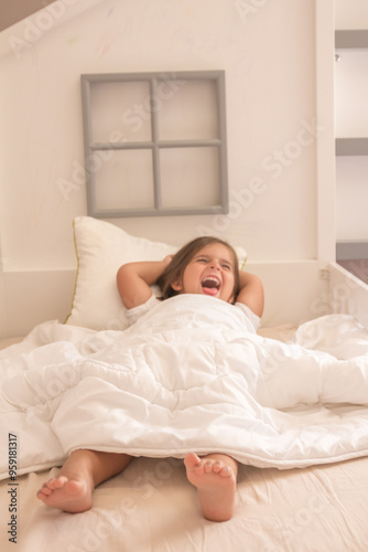 Little girl wrapped in a white blanket while sitting on the bed and smiling being tickled by dad