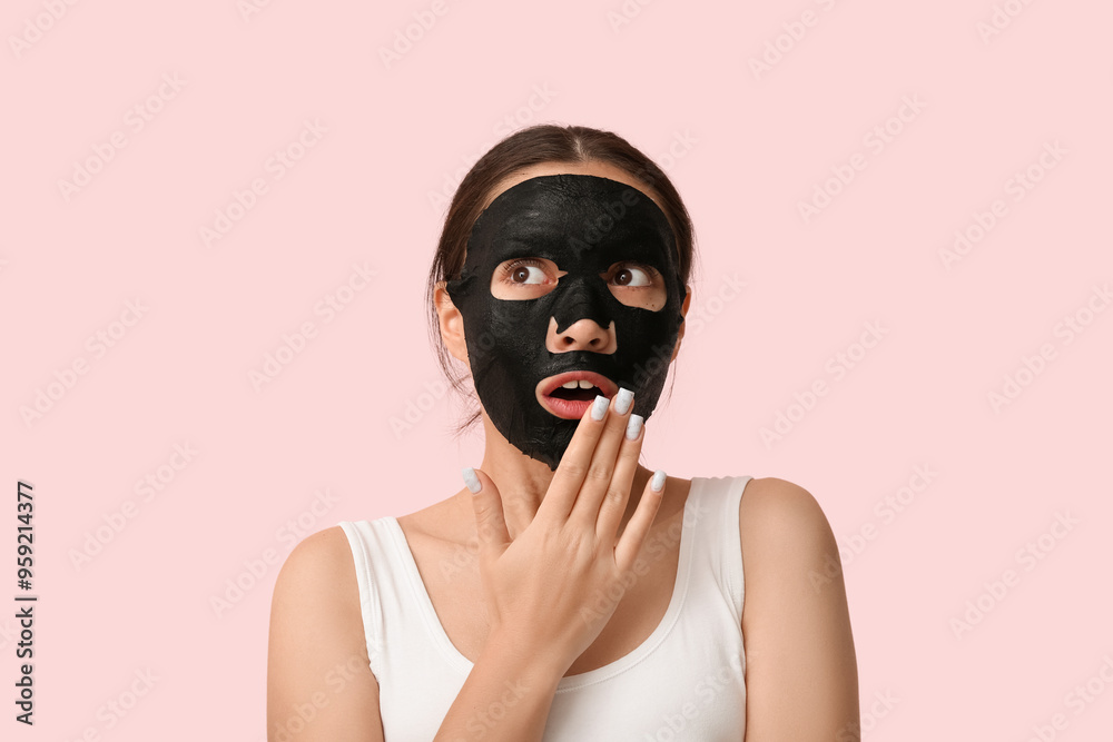 Surprised young woman with activated charcoal mask on her face against pink background Surprised young woman with activated charcoal mask on her face against pink background
