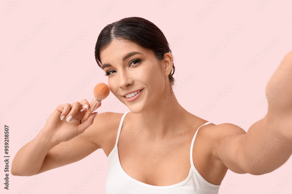 Beautiful young woman with makeup brush taking selfie on pink background Beautiful young woman with makeup brush taking selfie on pink background