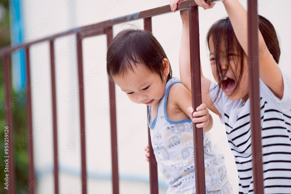 Obraz premium Cute boy playing climbing iron fences in the playground in summer with sisters, bright smiles of children, the love of sibling playing together happily. Excitement and fun come with a wide imagination