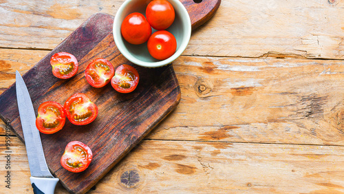 A wooden cutting board with a knife on it and a bowl of tomatoes