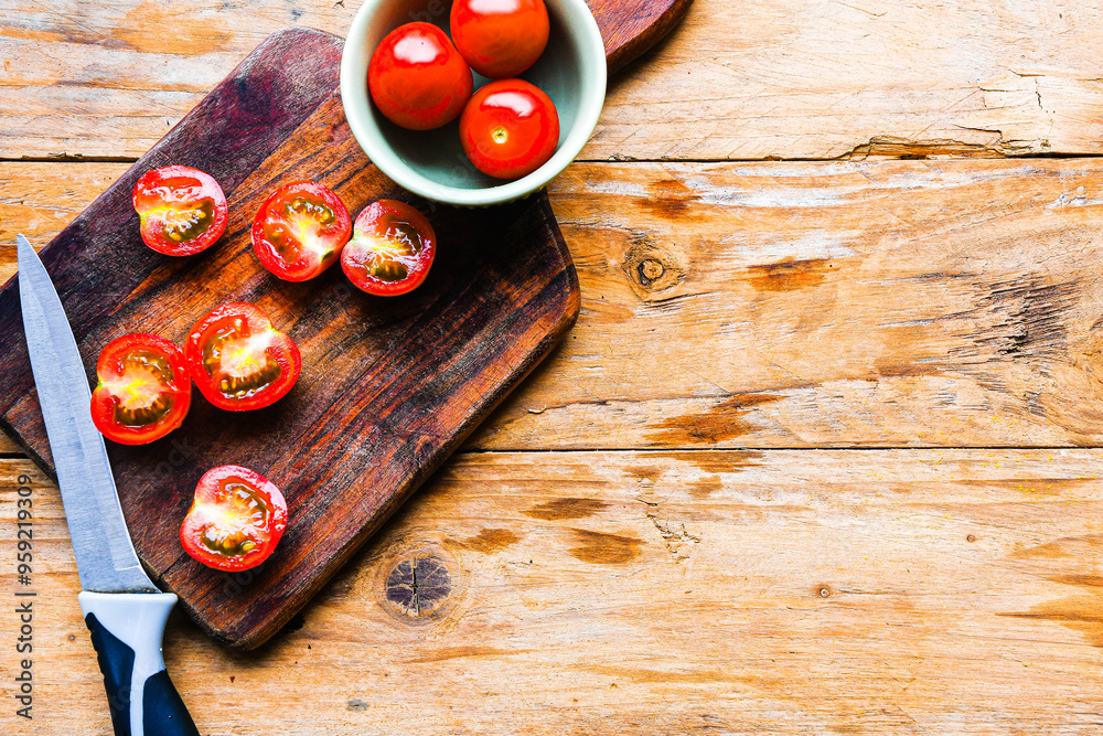 A wooden cutting board with a knife on it and a bowl of tomatoes A wooden cutting board with a knife on it and a bowl of tomatoes